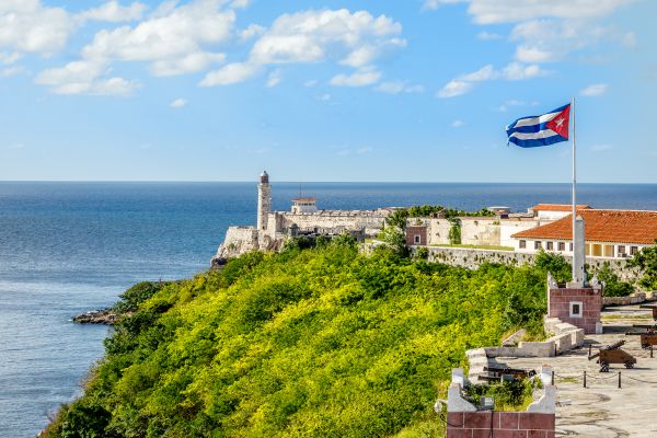 El Morro spanish fortress with lighthouse, cannons and cuban flag in th foreground, with sea in the background, Havana, Cuba