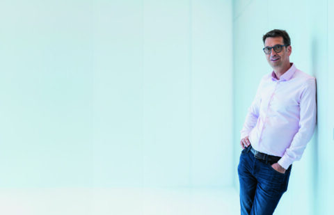 Porträt von Professor Uder, der lässig an eine Wand gelehnt in die Kamera blickt