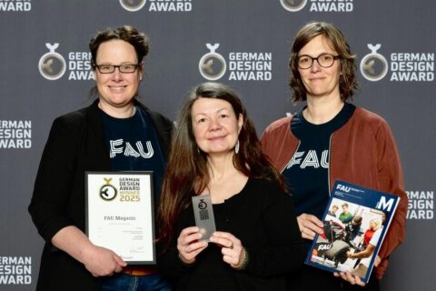 3 Frauen lächeln mit dem Entwurf in der Hand in die Kamera.
