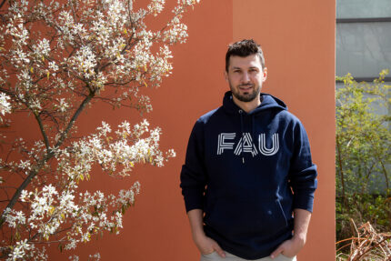 Prof. Rau, ein junger man kurzen dunklen Haaren, trägt einen Hoodie mit FAU-Logo.