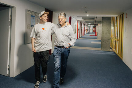Prof. Reif und Joachim Hornegger laufen Arm in Arm durch einen Gang in der WiSo. Sie unterhalten sich dabei.