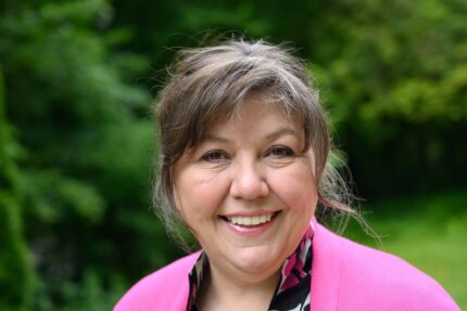 Portraitfoto draußen aufgenommen, im Hintergrund Grün