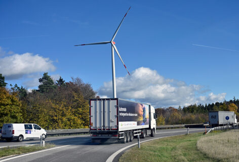 Ein Sattelschlepper auf der autobahn. Im Hintergrund eine Windturbine.