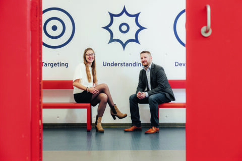 Die beiden sitzen auf roten Bänken.