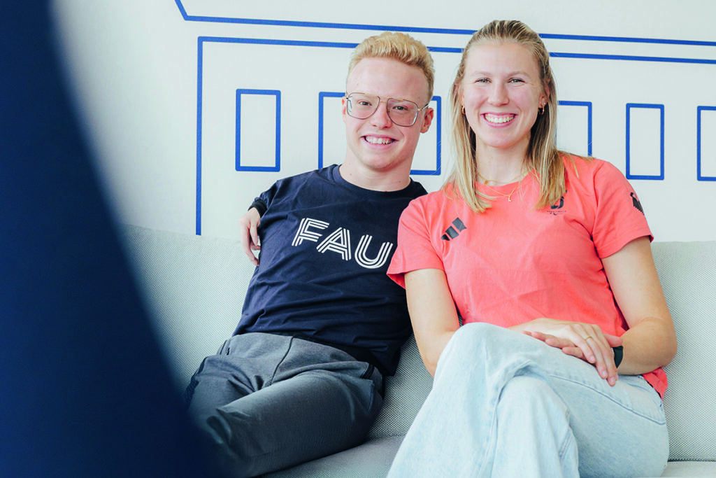 Josia Topf ein junger Mann mit blonden Haaren und Brille, und Lilly Sellak, eine junge frau mit blonden Haaren, sitzen gemeinsam auf einer Couch.